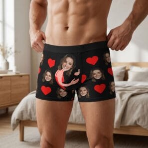 Personalized men’s black boxer briefs featuring a custom photo of a woman’s face integrated into a red heart hug illustration, surrounded by a repeating pattern of faces and red hearts.
